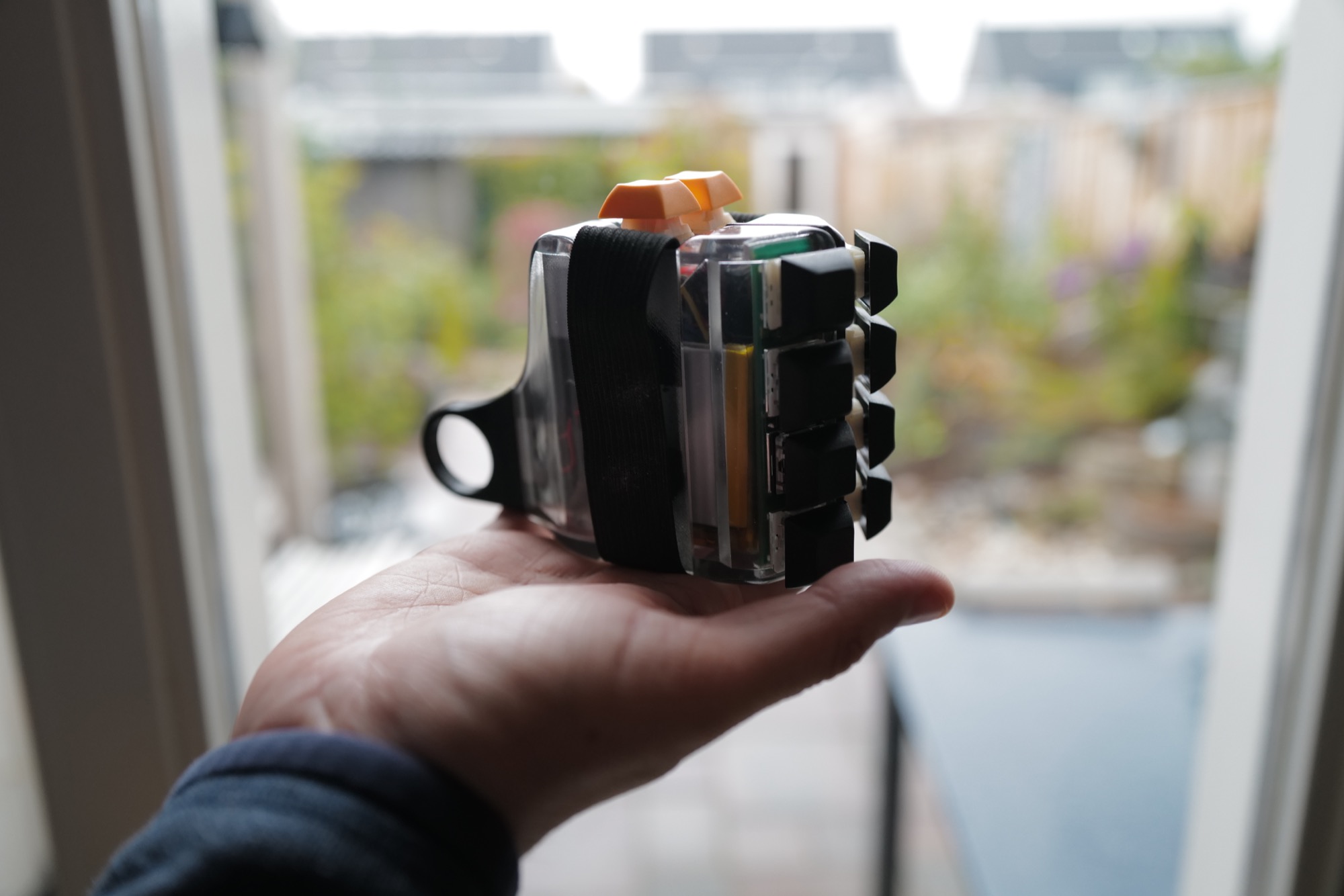 One half of the Wandering Computer held in an open hand, the clear shell showing the battery and keys.